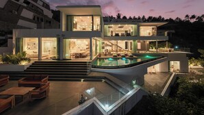 A modern multi-story house with a large outdoor pool, multiple balconies, and a staircase leading to the upper levels.