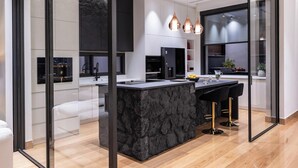 A modern kitchen with a stone island, black cabinets, and pendant lighting.