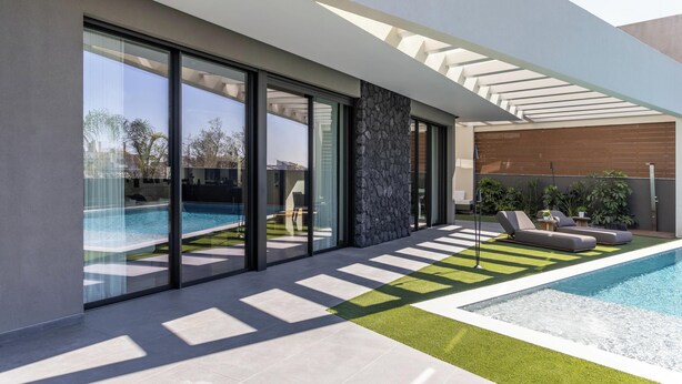 A modern house with a swimming pool, large glass doors, and a patio area with lounge chairs.