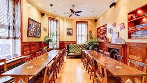 A dining area with a long wooden table, chairs, a green sofa, and wooden shelves with books and decorations.