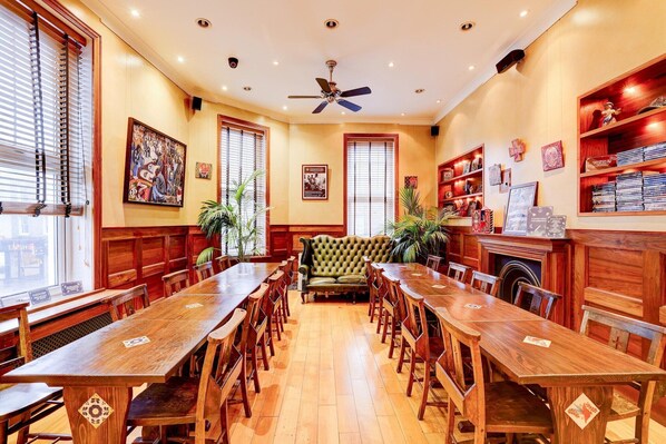 Un comedor con una larga mesa de madera, sillas, un sofá verde y estantes de madera con libros y adornos.