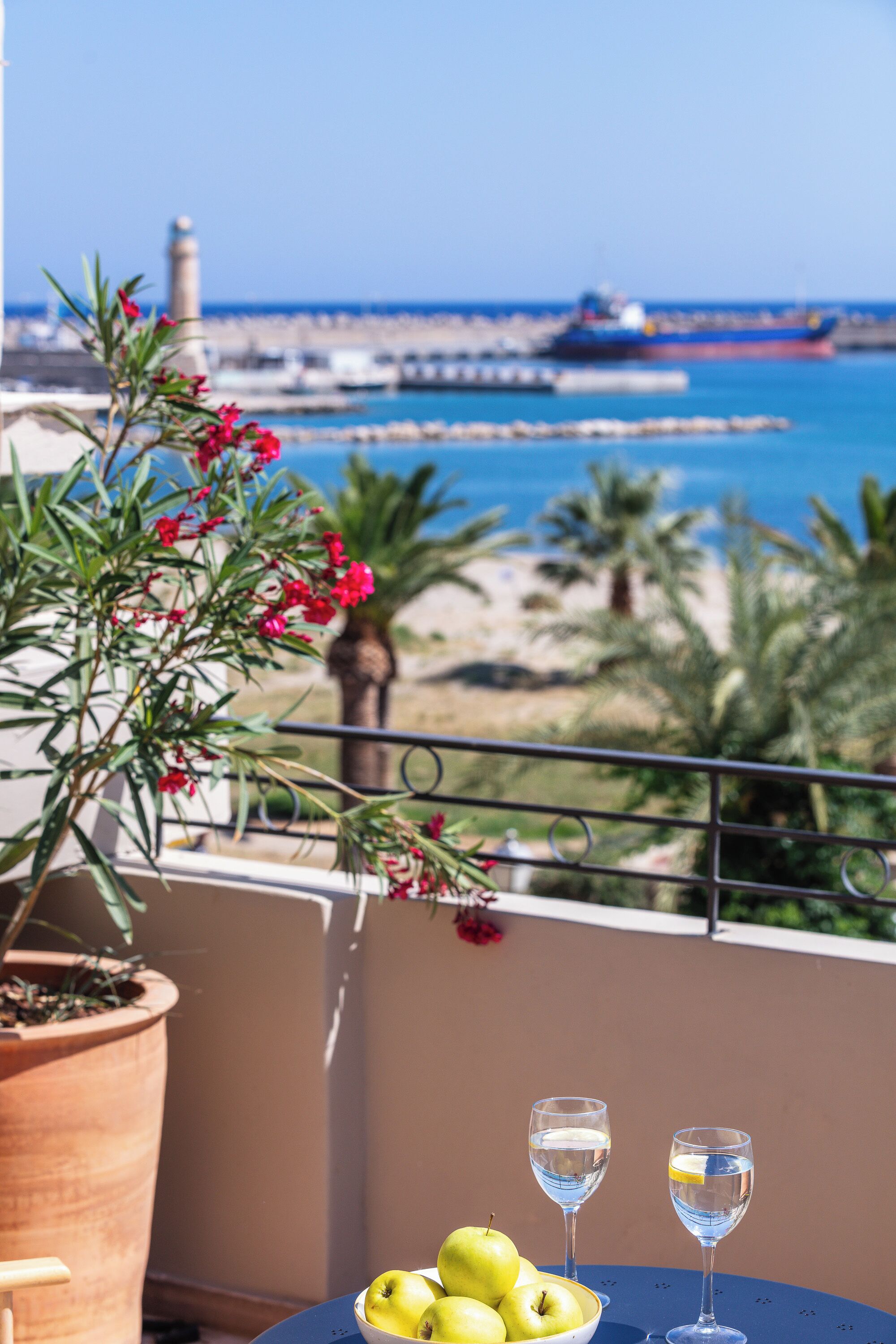 Ein Balkon mit Blick aufs Meer, einem Blumentopf und einem Tisch mit Äpfeln und Gläsern.