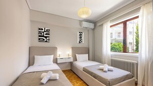A hotel room with two beds, a window with a view, and a ceiling light. - Seaside Secret Sea View Two Bedroom Apartment by BluPine (Athens)