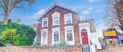A traditional brick building with a red door, white window frames, and a sign for Peckham Rooms Hotel.