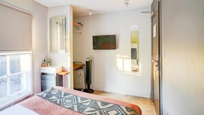 Ein Schlafzimmer mit Bett, Heizkörper, Fernseher, Fenster und Tür.