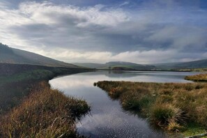 A serene landscape with a calm lake, surrounded by grassy hills and a cloudy sky.