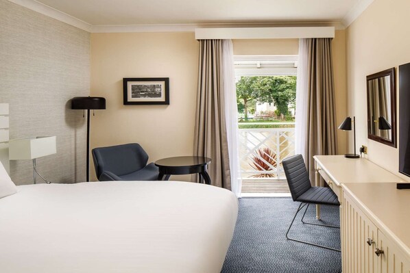 Habitación de hotel con cama, dos sillas, un escritorio, televisor y ventana con cortinas.
