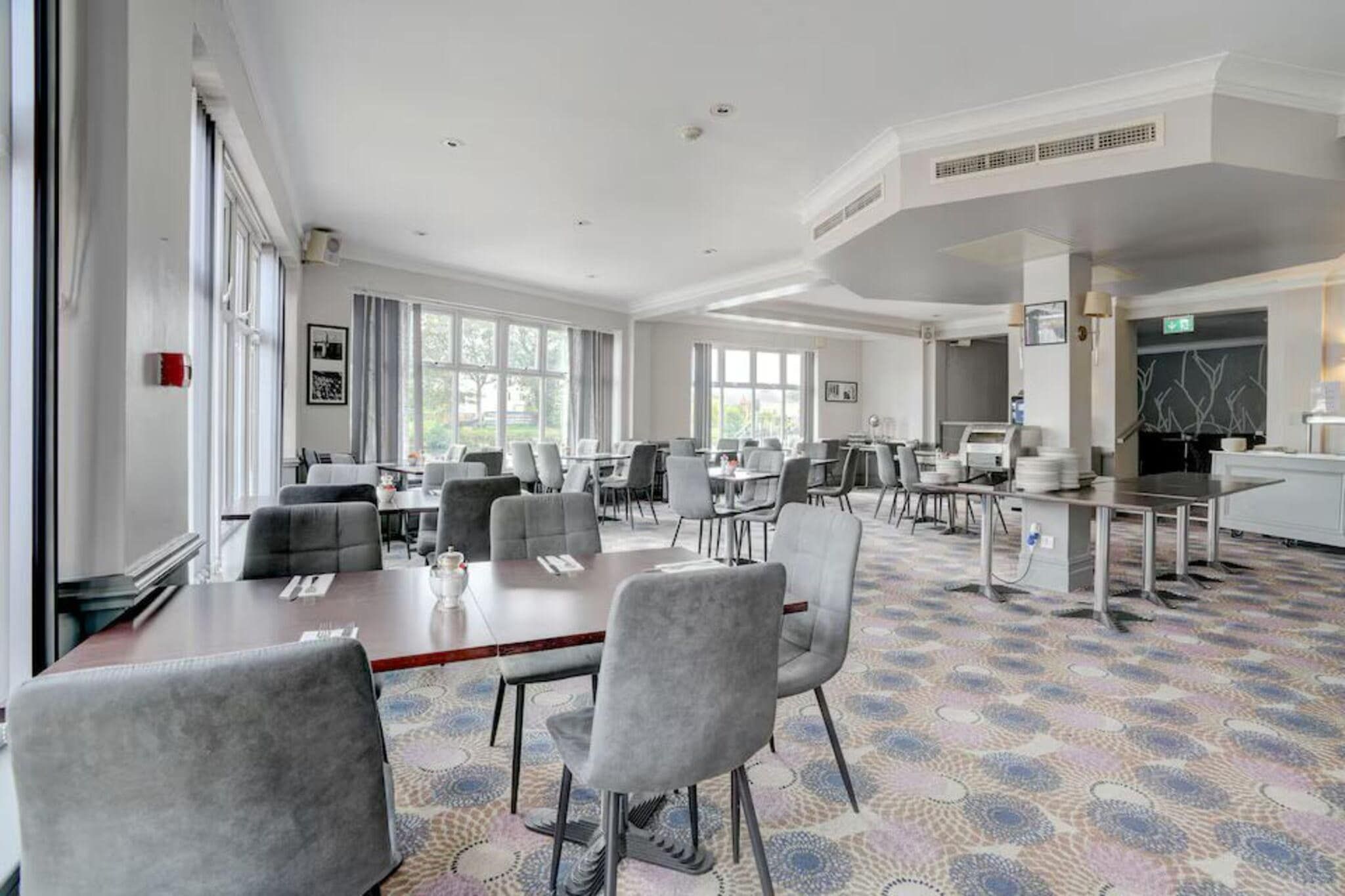 A spacious conference room with multiple tables and chairs, large windows, and a patterned carpet.