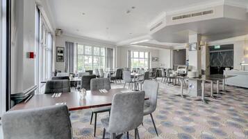 A spacious conference room with multiple tables and chairs, large windows, and a patterned carpet.
