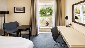 Ein Hotelzimmer mit Bett, Schreibtisch, Stuhl, einem kleinen Tisch und einem Fenster mit Vorhängen.