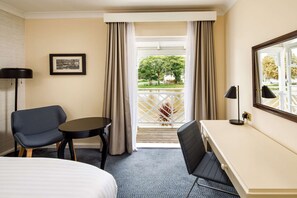 Una habitación de hotel con cama, escritorio, silla, una mesita y ventana con cortinas.