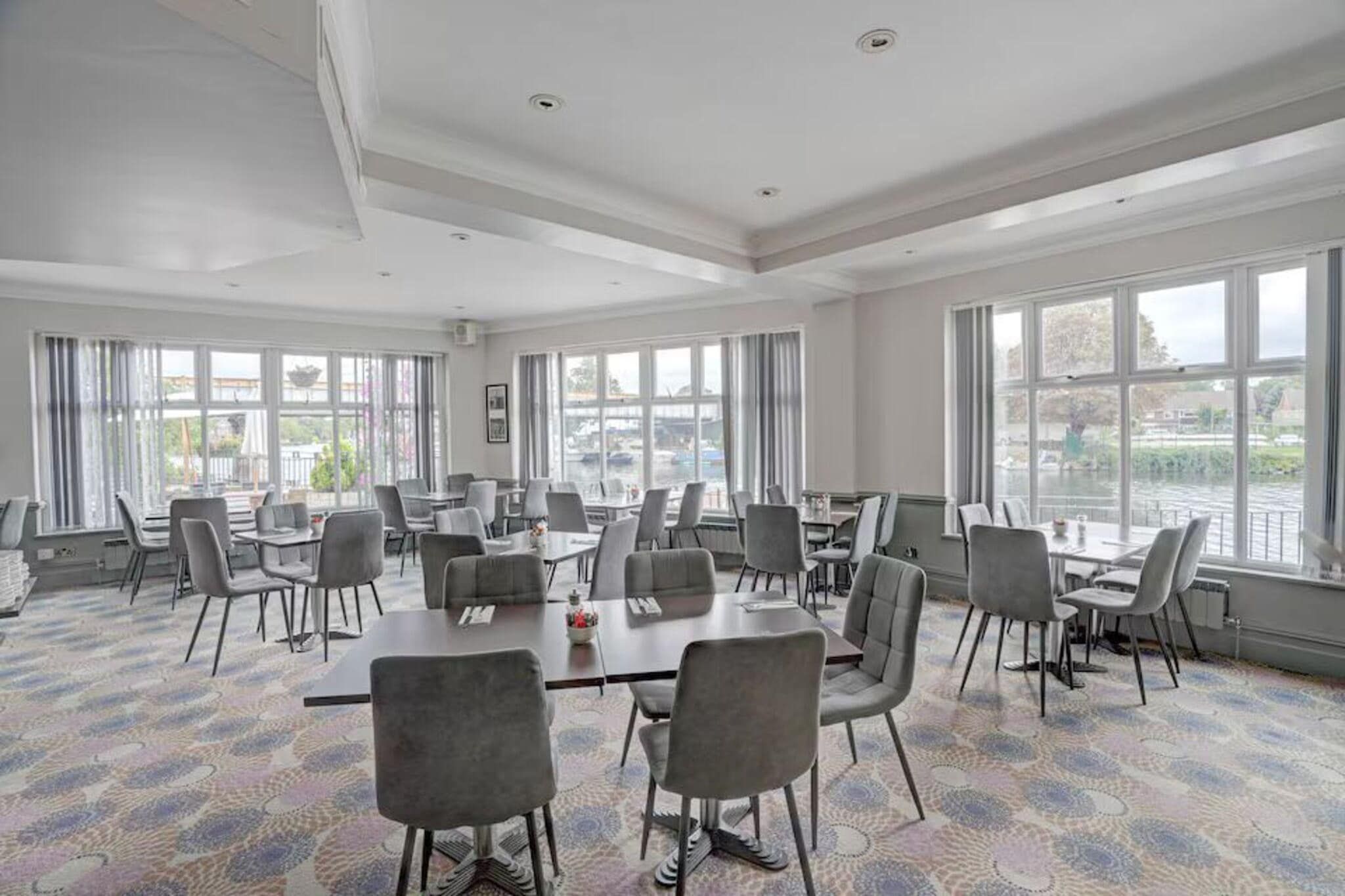 A conference room with multiple tables and chairs, large windows, and a view of the outside.