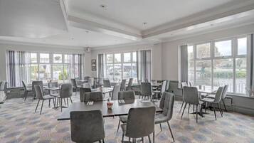 A conference room with multiple tables and chairs, large windows, and a view of the outside.
