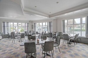 Une salle de conférence dotée de plusieurs tables et chaises, de grandes fenêtres et offrant une vue sur l’extérieur.
