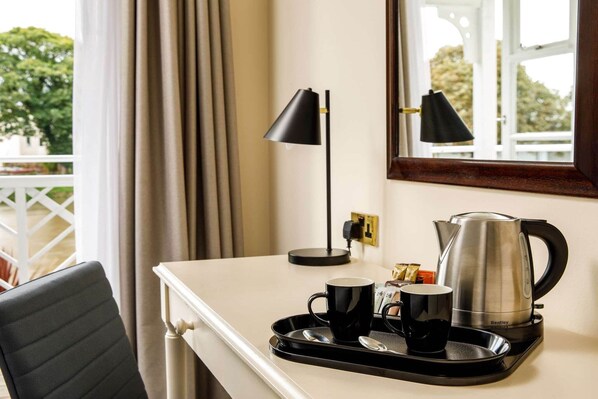Una habitación de hotel con escritorio, tetera, dos tazas y bandeja.