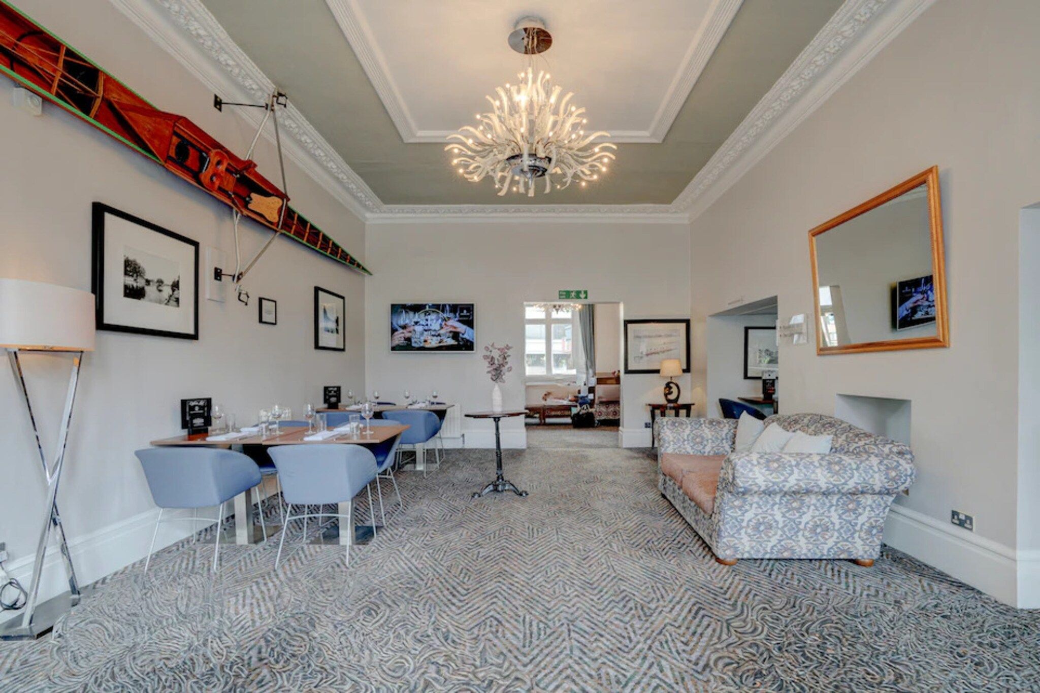 Una camera d'albergo con zona pranzo, tappeto decorato, lampadario e opere d'arte appese alle pareti.