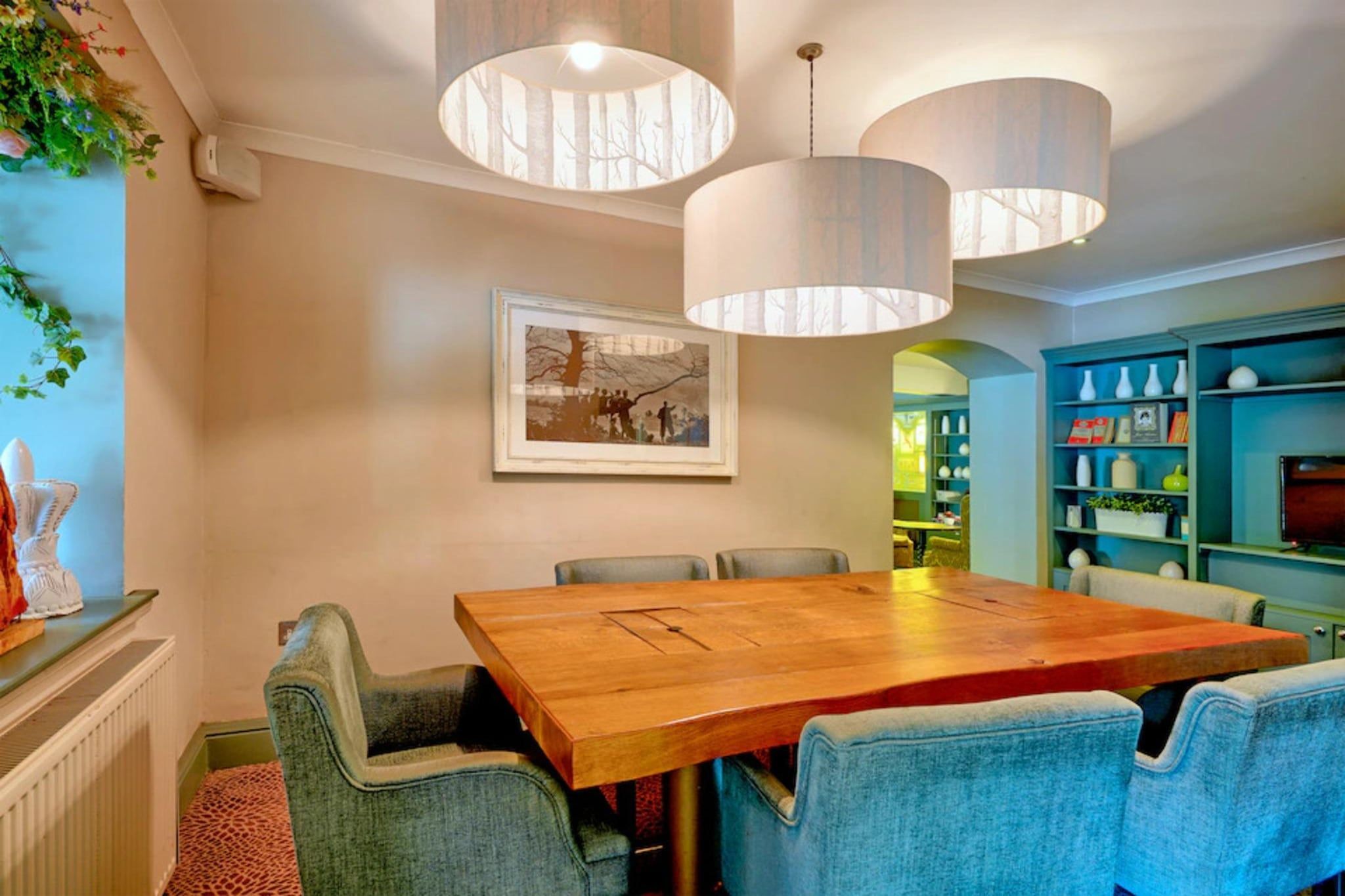 A dining area with a wooden table, blue upholstered chairs, and pendant lighting.