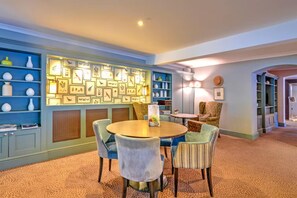 A cozy room with a round table and chairs, a bookshelf with framed pictures, and a patterned carpet. - Sunday Box Hill Burford Bridge - Standard Double Room (Dorking)