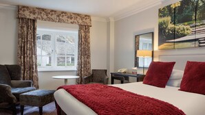 Una habitación de hotel con una cama grande, un escritorio, una silla y una ventana con cortinas.