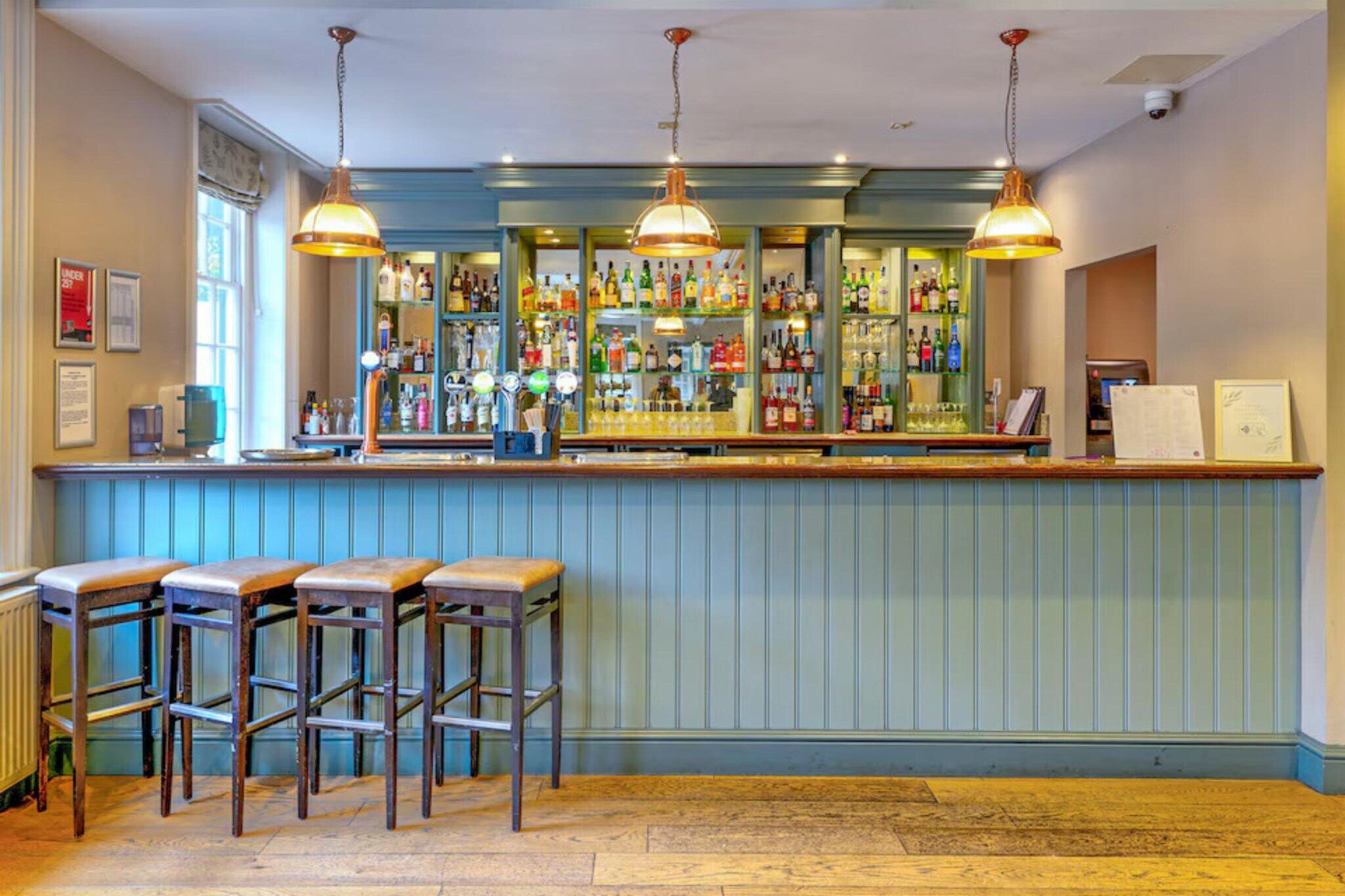 Een bar met krukken, een toonbank en hangende lampen.