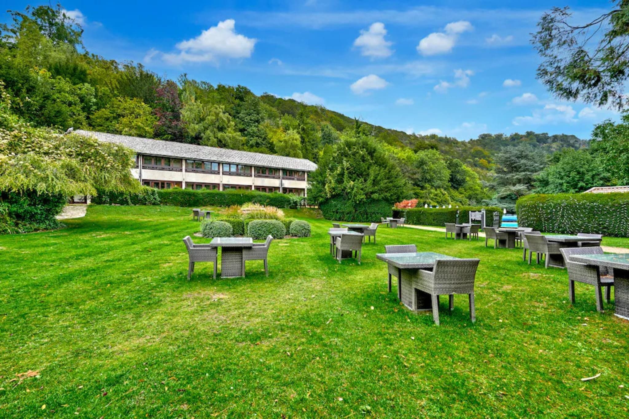 Een terras met tafels en stoelen, een gebouw op de achtergrond en een heuvellandschap.