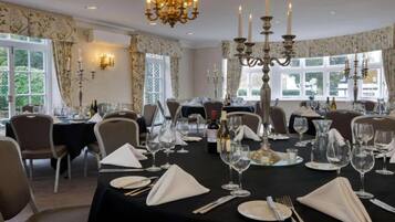 A formal dining room with tables set for a meal, chandeliers, and large windows.