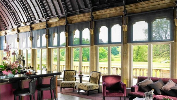 A spacious room with a bar area, seating, and large windows offering a view of a garden. - Sunday Walton Hall Retreat & Spa | Standard Double (Wellesbourne Hastings)