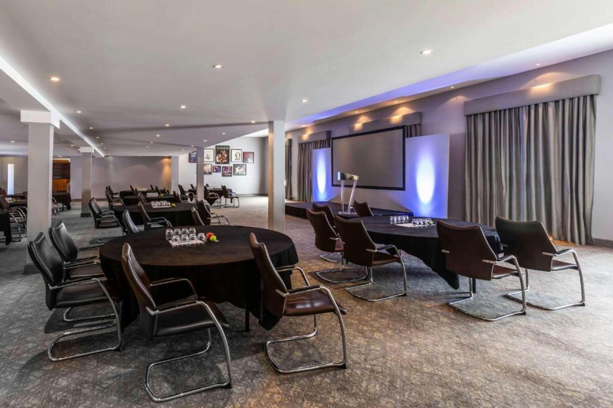 Een vergaderzaal met een grote ronde tafel, meerdere stoelen, een scherm voor een projecteur, en een zithoek met gordijnen.