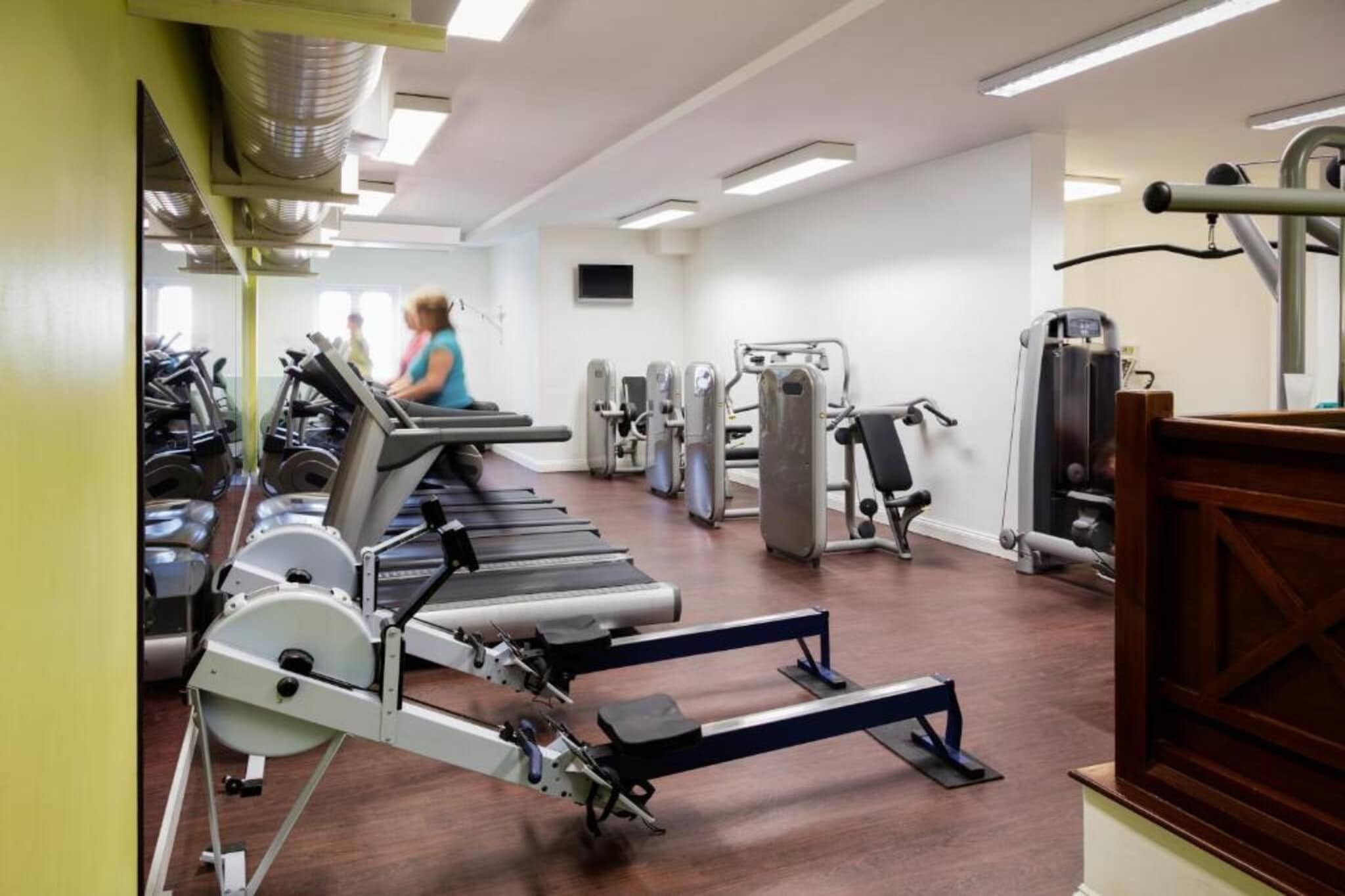 Un gimnasio con cintas de correr, máquinas de pesas y un espejo grande.