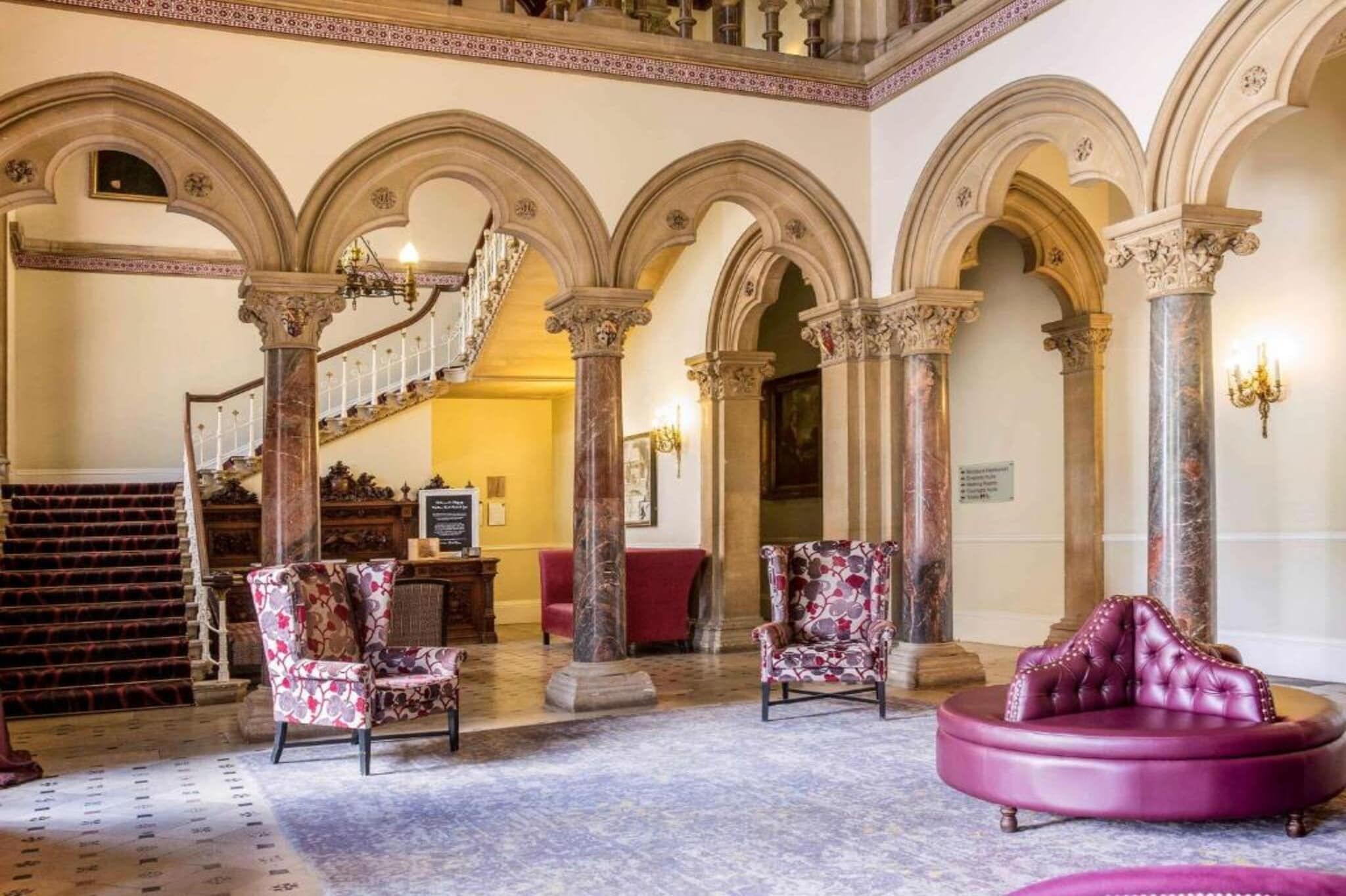A grand lobby with a staircase, ornate columns, and plush seating.