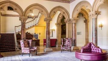 A grand lobby with a staircase, ornate columns, and plush seating.