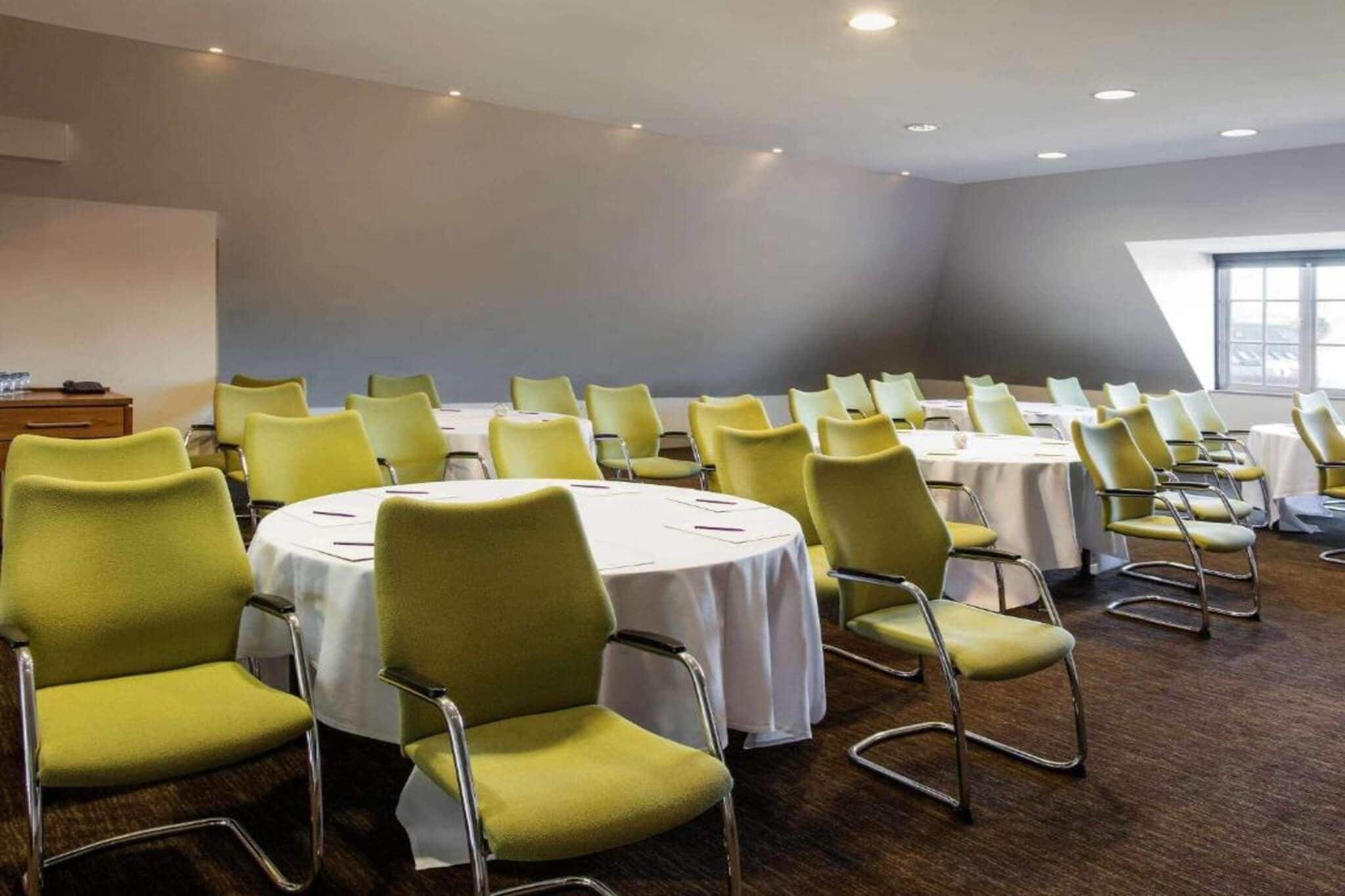 A conference room with round tables and chairs, a wooden cabinet, and a large window.