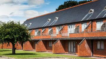 Fileira de edifícios de tijolo com janelas salientes e uma árvore em primeiro plano.