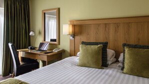 A hotel room with a bed, a desk, a chair, a lamp, a mirror, and a window with curtains. - Sunday Walton Hall Retreat & Spa | Standard Double (Wellesbourne Hastings)