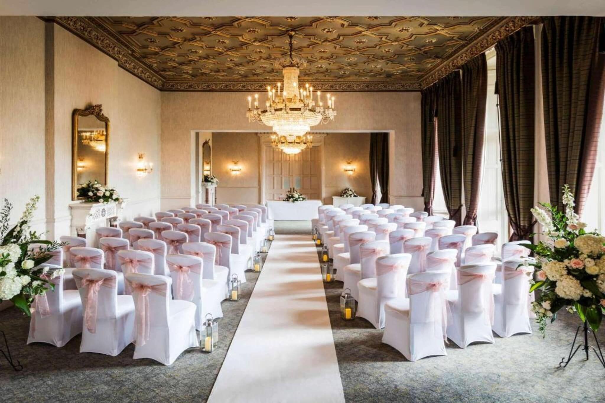 Un espacio para eventos formales con filas de sillas, un pasillo central y una araña.