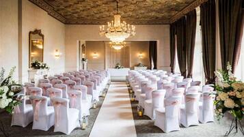Un espacio para eventos formales con filas de sillas, un pasillo central y una araña.