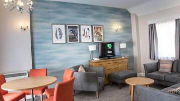 Habitación de hotel con zona de estar, televisor y obra de arte en la pared.