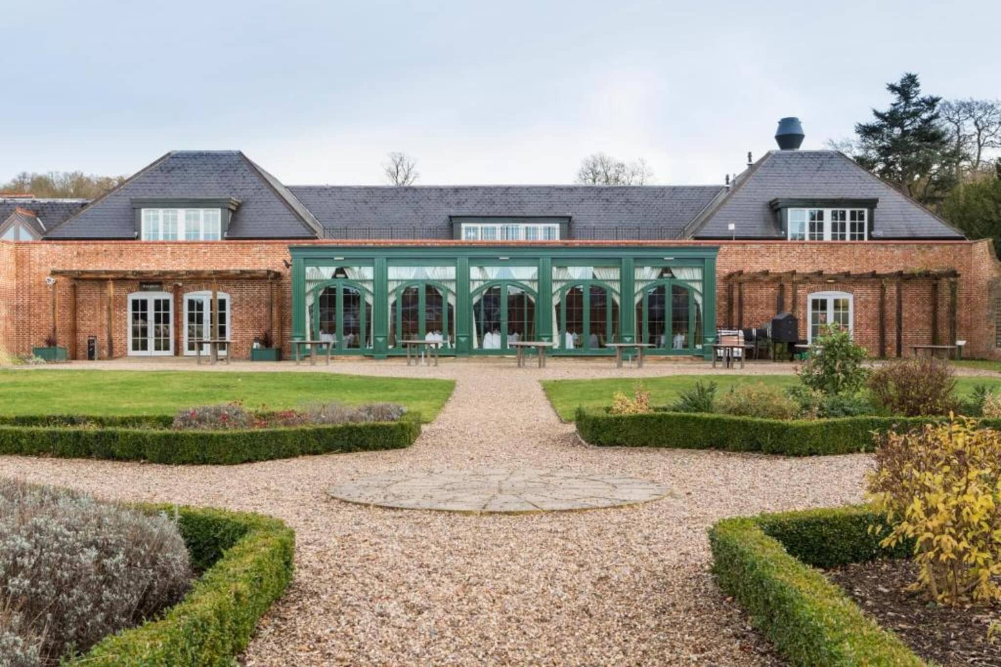 A brick building with a central glass conservatory, a gravel pathway, and formal garden landscaping.