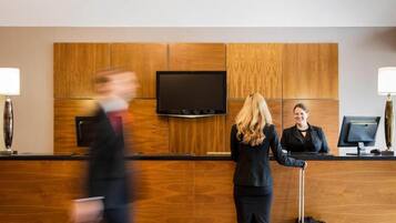 Un mostrador de recepción de hotel con un televisor de pantalla plana, paneles de madera y dos lámparas.