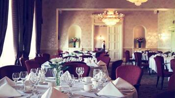 Een stijlvolle eetzaal met gedekte tafels, elegante tafeldecoraties en een kroonluchter.