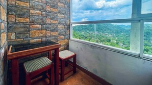 A room with a stone wall, a window with a view of a green landscape, and a wooden table with two chairs. - The Heritage Inn  (Kandy)