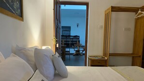 A hotel room with a bed, pillows, a nightstand, and a wooden wardrobe. - The Heritage Inn  (Kandy)