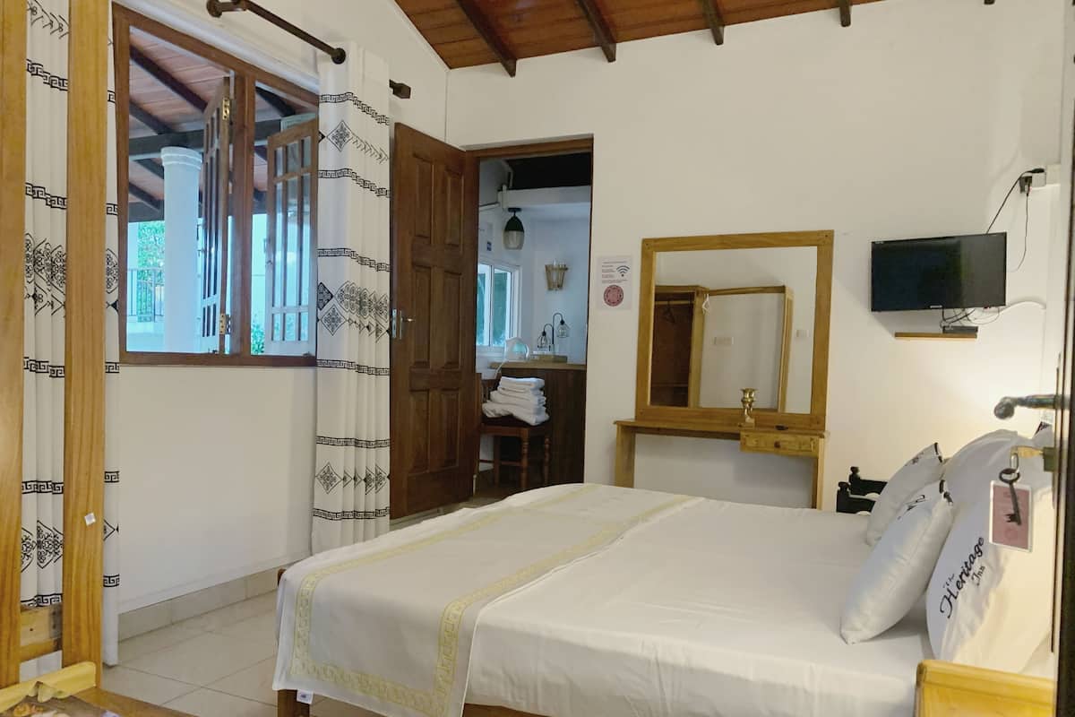 A bedroom with a bed, a wooden nightstand, a TV, and a mirror.