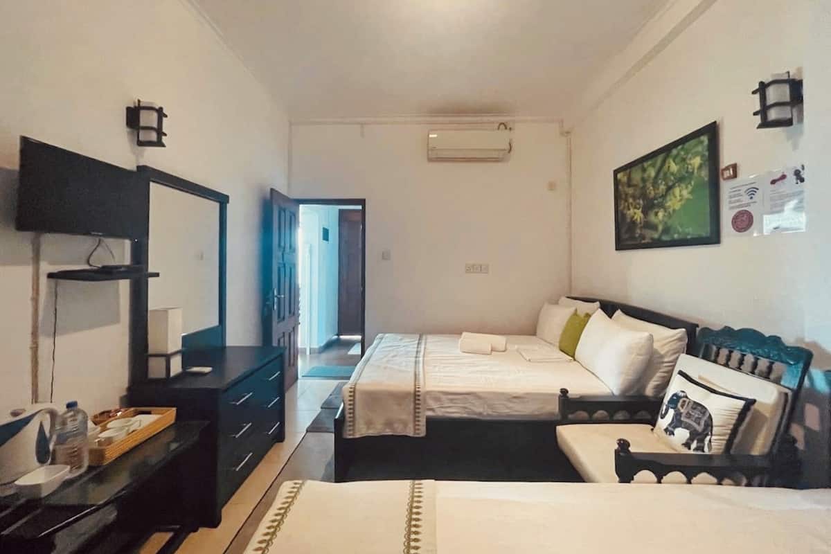 A hotel room with two beds, a desk with a chair, a flat-screen TV, and a painting on the wall.