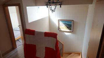 A staircase with a wooden handrail, a red and white blanket draped over it, and a framed painting on the wall.