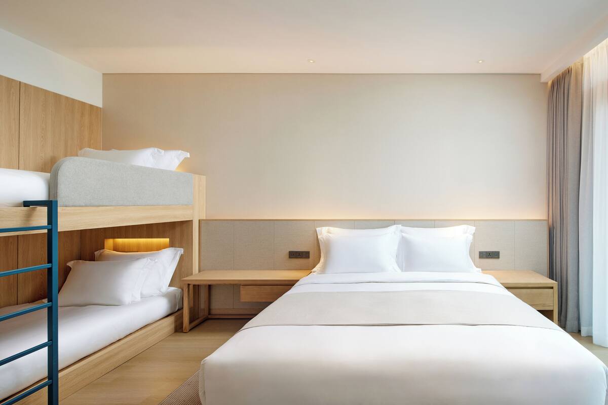 A hotel room with a bunk bed, a single bed, a bedside table, and a nightstand.
