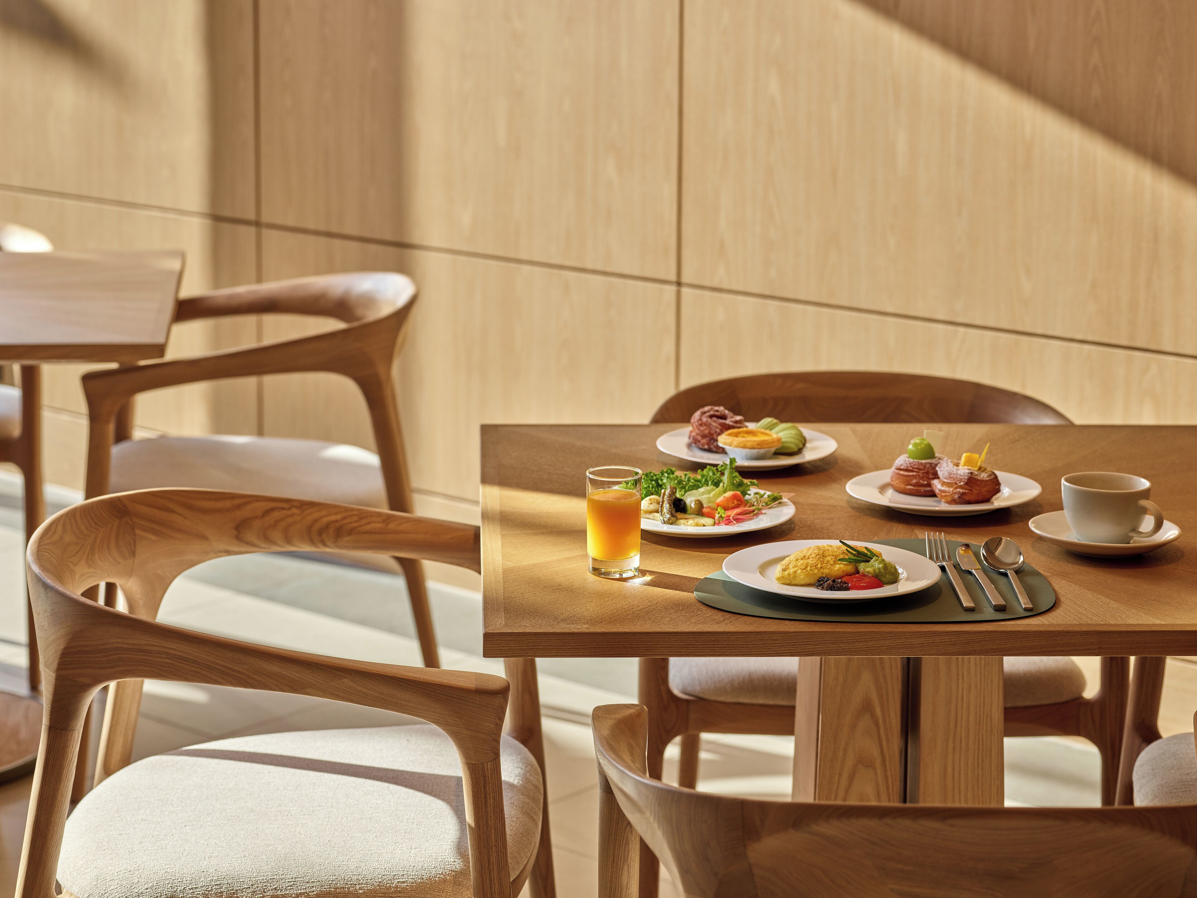Un comedor con muebles de madera y una mesa dispuesta con platos de comida, un vaso de jugo y cubiertos.