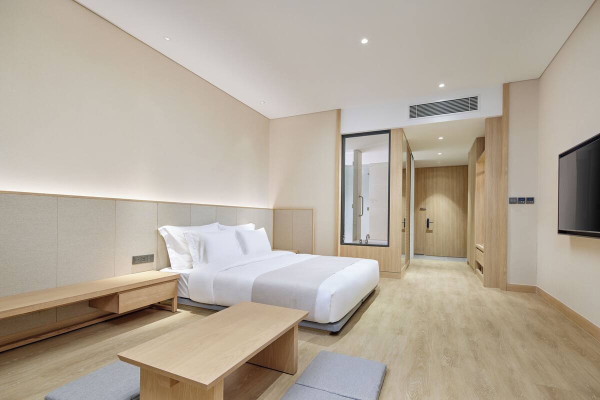 A modern hotel room with a bed, bedside table, and a TV mounted on the wall.