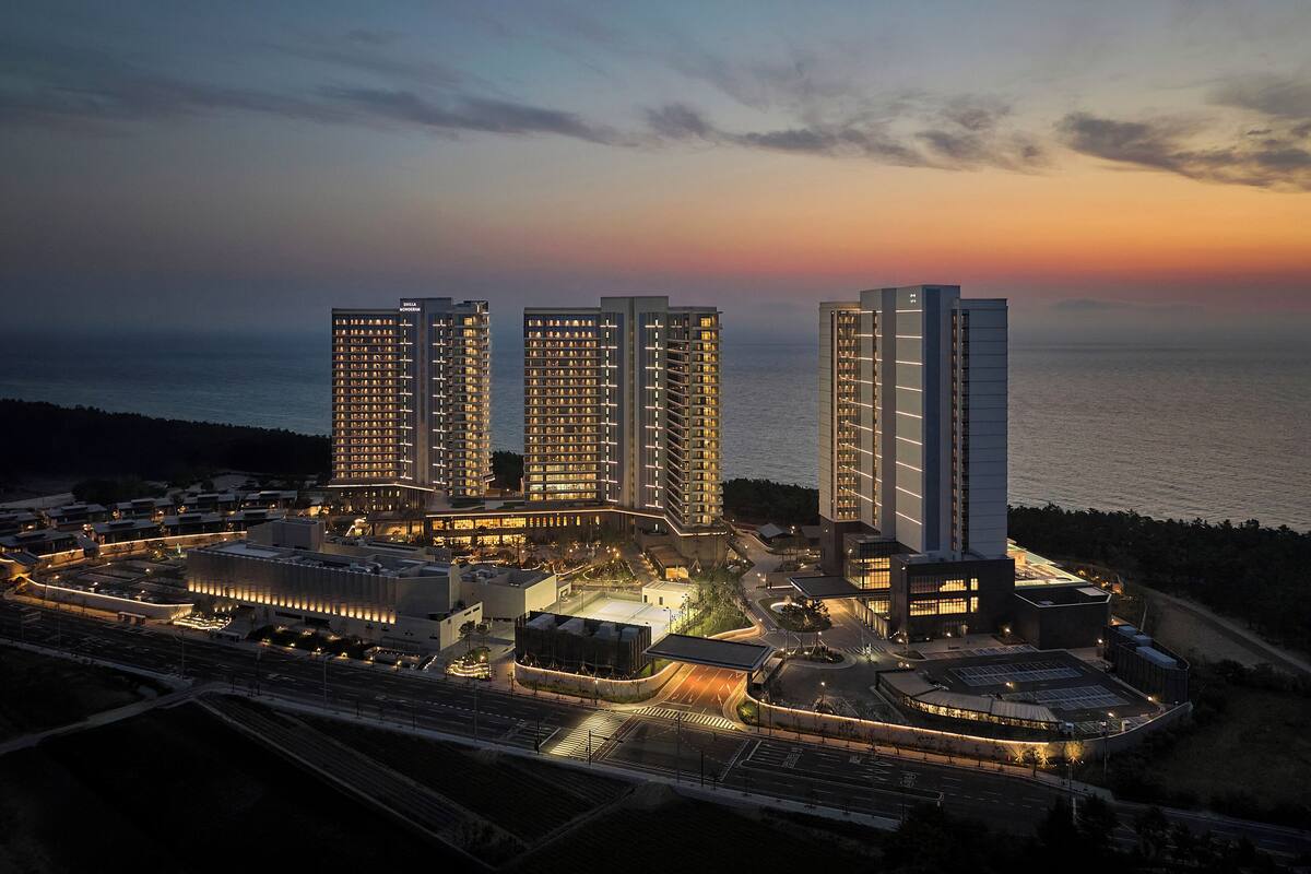 A high-rise hotel complex with multiple buildings, a well-lit parking area, and a view of the sea at dusk.