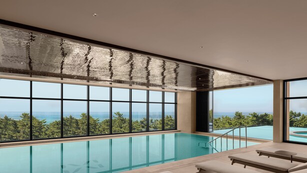 Ein moderner Innenpool mit großen Glaswänden, Liegestühlen und Meerblick.